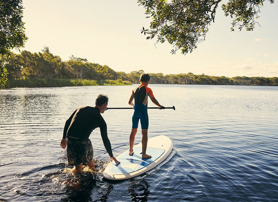 man pushing boy balancing on stand-up paddleboard on a lake