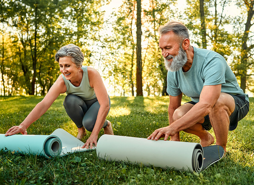 two older people rollling out yoga mats outdoors